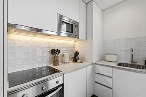Eine kleine Küche mit Mikrowelle, Toaster und Herd, mit weißen Schränken und einer gefliesten Spritzschutzwand.