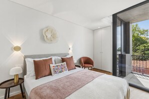 Un dormitorio moderno con una cama grande, dos mesitas de noche, una lámpara fijada a la pared y vistas a través de una puerta de cristal.