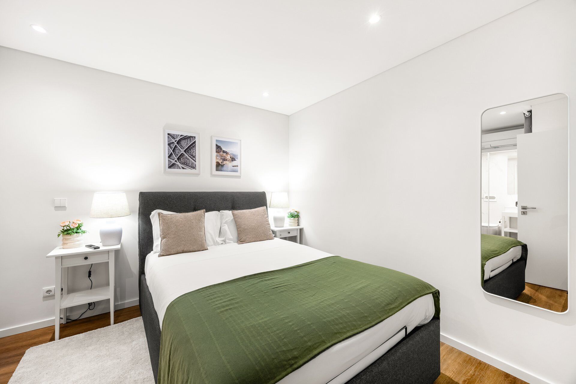 A modern bedroom with a bed, bedside tables, a mirror, and artwork on the wall.