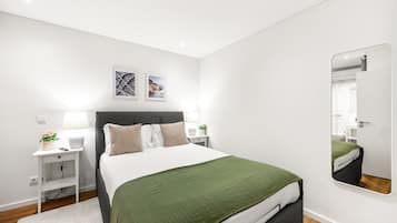 A modern bedroom with a bed, bedside tables, a mirror, and artwork on the wall.