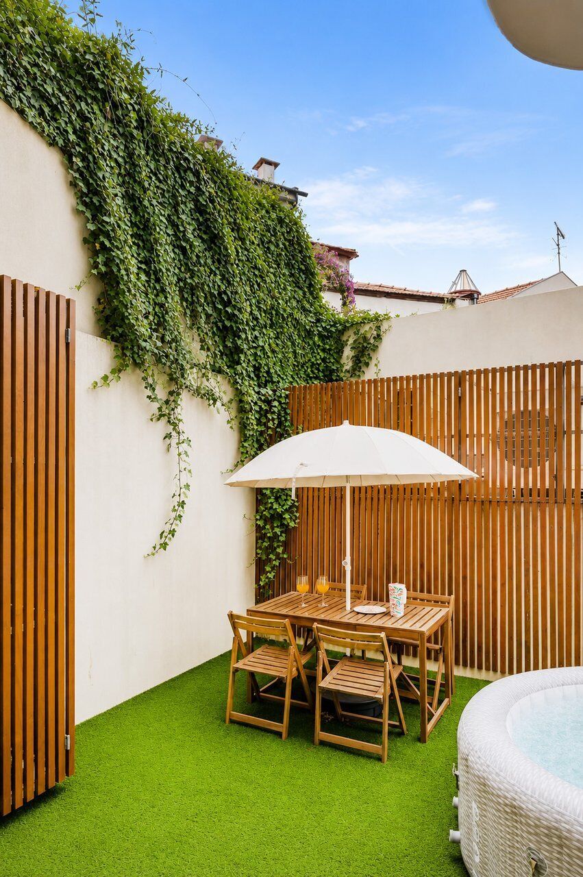 Eine Terrasse mit Tisch und Stühlen, einem weißen Sonnenschirm und einem Whirlpool.