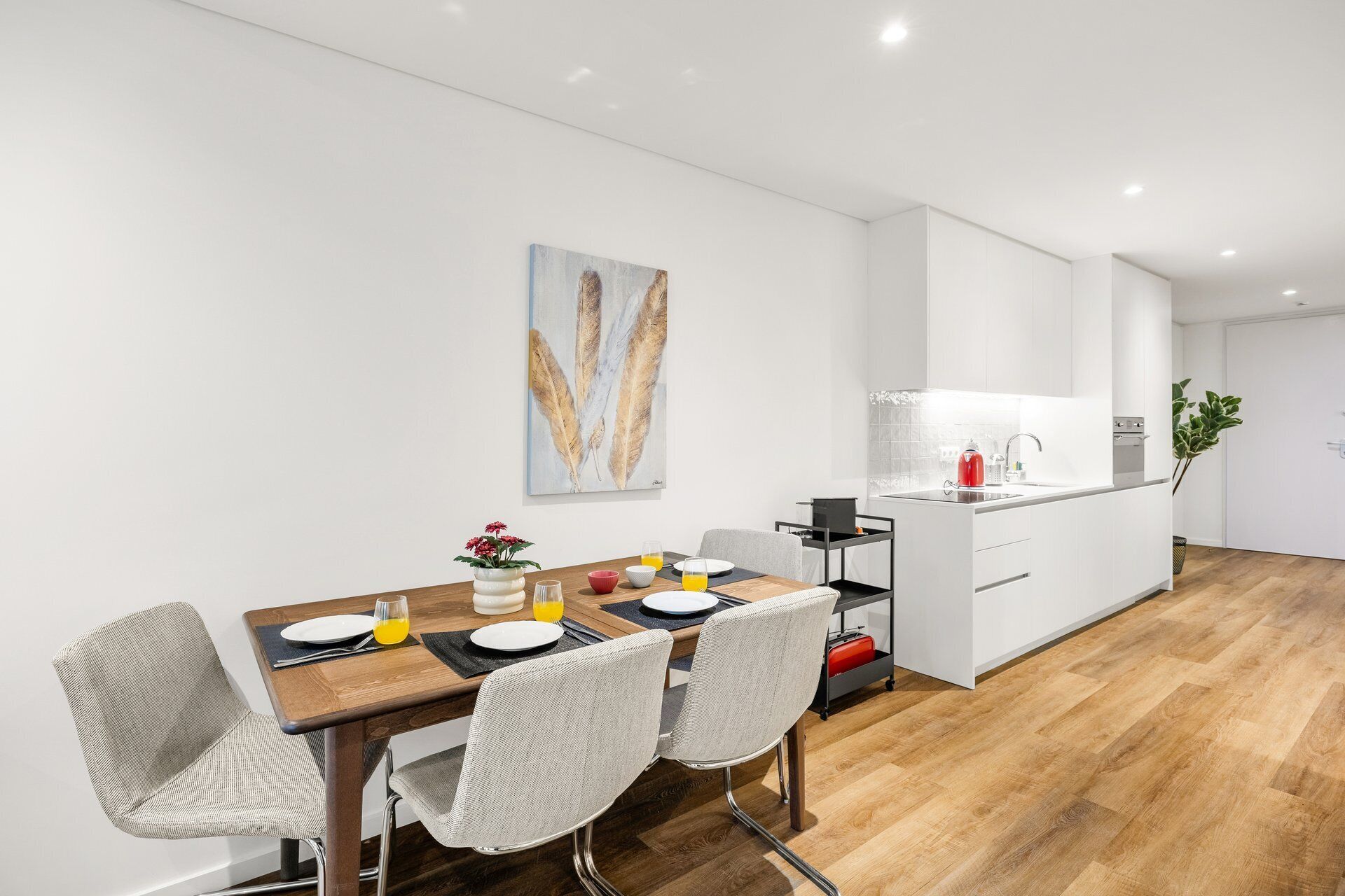 Eine moderne Küche mit weißen Schränken, einem Holztisch mit vier Stühlen und einem Bild an der Wand.