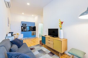 A modern living room with a sofa, a TV on a wooden cabinet, and a kitchen in the background. - Balcony City Views | Porto (Porto)