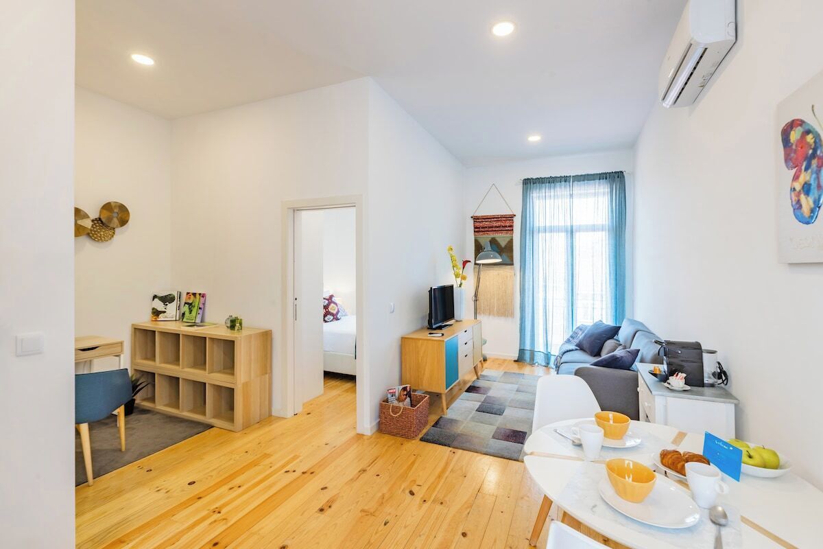 A modern living room with a wooden floor, a dining table with breakfast items, a sofa, and a TV stand.