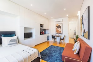 A modern bedroom with a bed, a sofa, a dining area, and a kitchen. - Stylish Studio w/ AC | Central Porto (Porto)