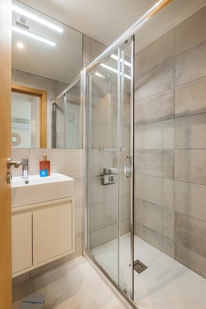 A modern bathroom with a glass shower enclosure, a sink with a soap dispenser, and a mirror. - Urban Style in Bonfim | Porto (Porto)