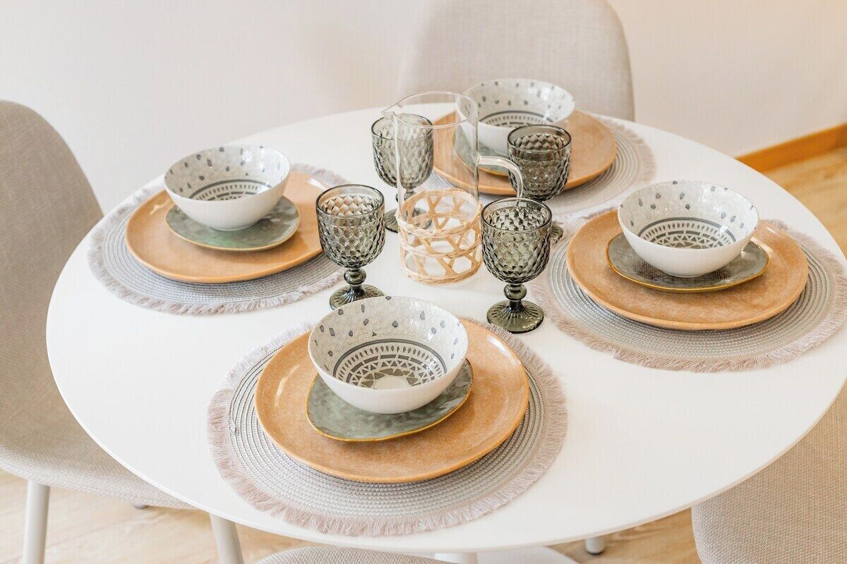 A round dining table with six bowls, a pitcher, and a woven centerpiece.