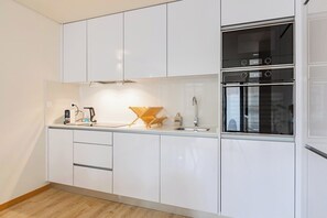 Eine moderne Küche mit weißen Schränken, einem eingebauten Ofen und einer Arbeitsplatte mit Wasserkocher und Küchengerät.