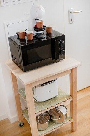 A kitchen with a microwave on a wooden stand, a white appliance below, and a door with a handle. - City Pocket | 111 Collection (Porto)