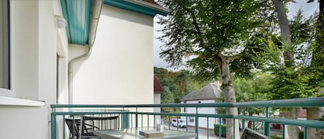 A balcony with a table and chairs, a view of the street, and a tree.