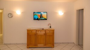 A hotel room with a wooden cabinet, a wall-mounted TV, two wall sconces, a clock, and a door. - Apartment '22 Anemone' with Balcony and Wi-Fi (Zempin)
