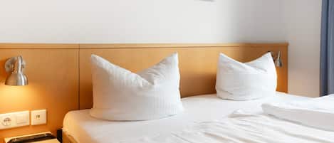 Une chambre d’hôtel avec une tête de lit en bois, deux oreillers blancs, une lampe de chevet et une table de chevet avec une lampe, ainsi qu’un tableau accroché au mur.