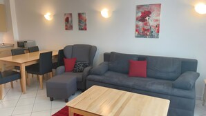 A modern living room with a grey sofa, red cushions, a wooden coffee table, and a dining area with a table and chairs. - Apartment '22 Anemone' with Balcony and Wi-Fi (Zempin)