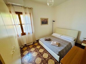 A bedroom with a bed, a nightstand, a picture on the wall, and a patterned floor.
