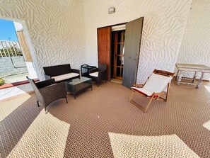 Ein Zimmer mit einem gemusterten Boden, einem Sofa, einem Sessel, einem Tisch und einer zur Außenseite führenden Tür.