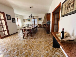 A dining area with a patterned floor, a long table, chairs, a chandelier, and a wine bottle on a table.