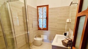 Un baño con cabina de ducha de vidrio, bañera, lavamanos con espejo y ventana.