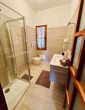 A bathroom with a glass shower enclosure, a bathtub, a sink with a mirror, and a window.