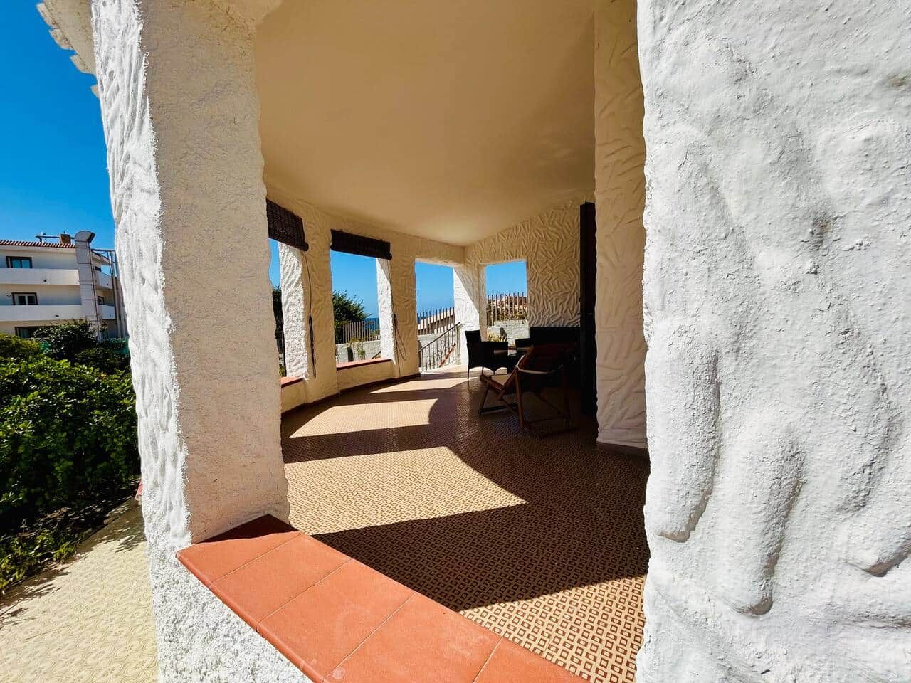 Un espace extérieur abrité, aménagé avec des sièges, offrant une vue sur la mer et avec un bâtiment visible à l’arrière-plan.