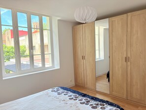 A bedroom with a large bed, a wardrobe, and a window with a view of a building and greenery. - House in the city center with parking, a garden, and a pool (Aix-en-Provence)