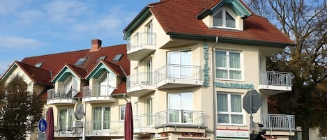 Un edificio de varios pisos con balcones, un letrero que dice 'WALDAUS' y varias tiendas, incluyendo 'Ristorante' y 'Marco Polo'.
