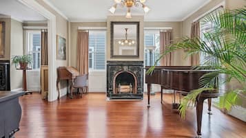 A spacious room with hardwood flooring, a grand piano, a fireplace, and a large mirror.