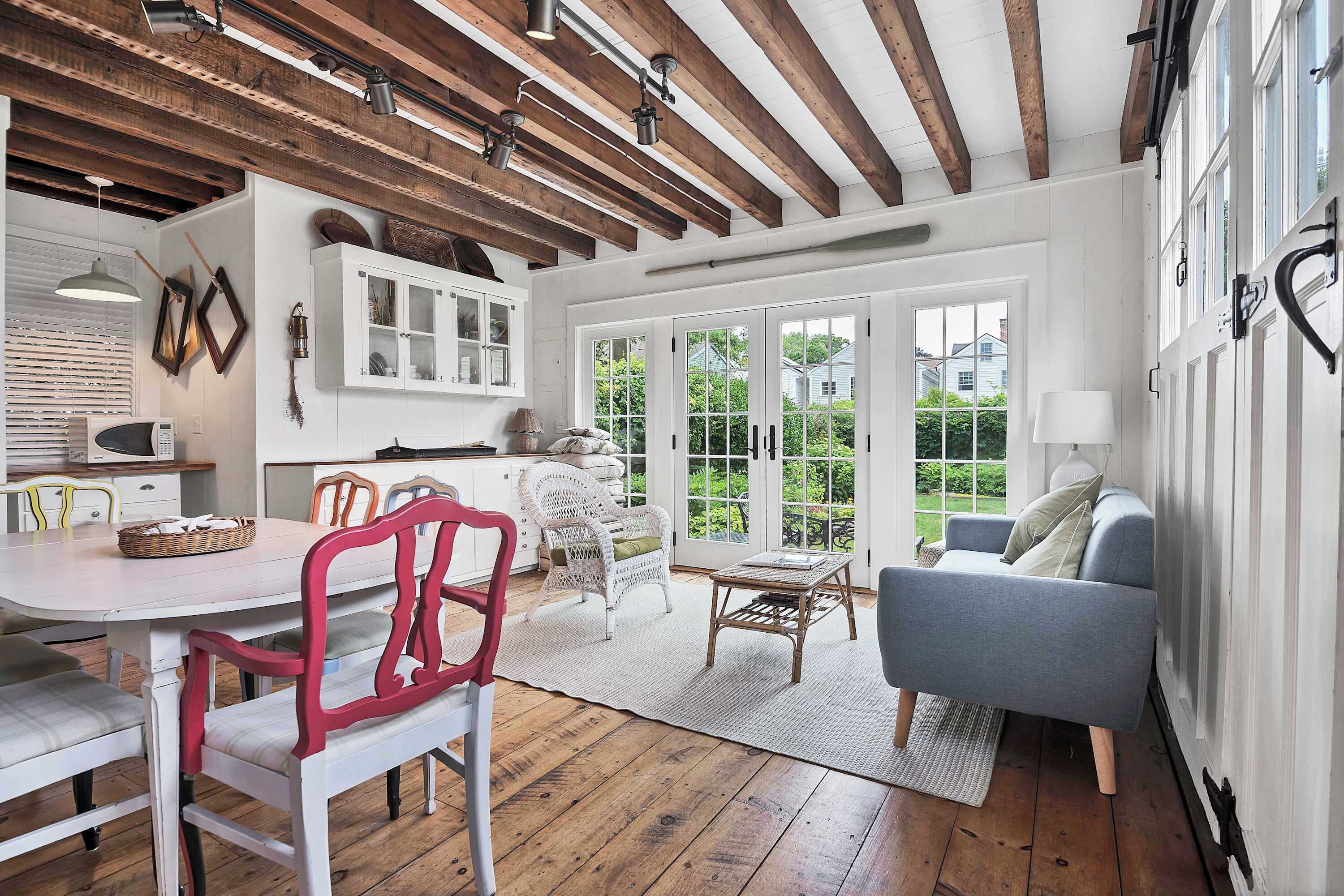 A spacious room with a wooden ceiling, white walls, a dining area with a table and chairs, a sofa, and a view through large windows.