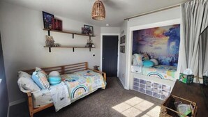 A cozy room with a bed, a small table, a shelf with items, and a door. - The Hive Hideaway (Meridian)