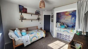 A cozy room with a bed, a small table, a shelf with items, and a door. - The Hive Hideaway (Meridian)