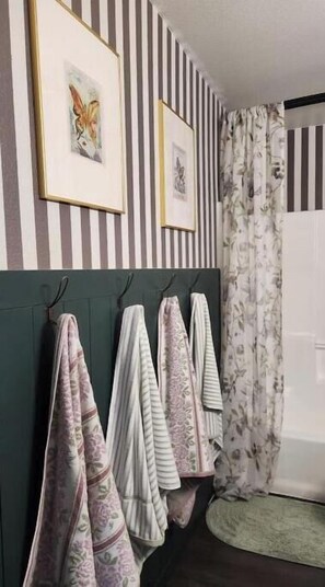 A bathroom with striped walls, a headboard with towels, and framed artwork. - The Hive Hideaway (Meridian)