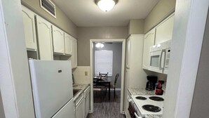 A narrow kitchen with white cabinets, a refrigerator, a microwave, and a stove. - Cozy Lakeside Two Bedroom Escape (Wichita)