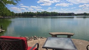 A lakeside view with a table and chair, a stone bench, and a red chair. - Cozy Lakeside Two Bedroom Escape (Wichita)