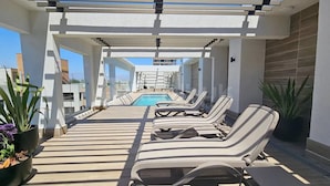A rooftop pool area with lounge chairs, a pool, and potted plants. - Rbk Cómodo Studio con gran ubicación (Santiago)