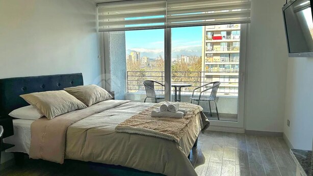 A bedroom with a bed, a balcony with a table and chairs, and a city view. - Rbk Cómodo Studio con gran ubicación (Santiago)