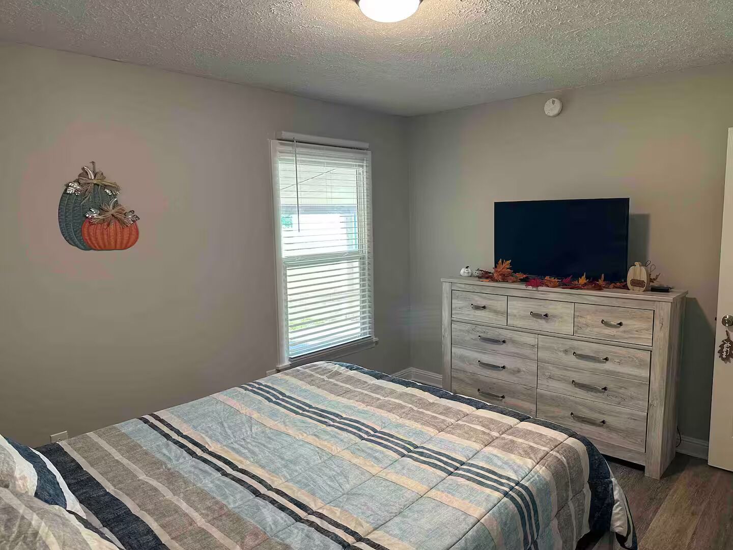 Quarto com cama, cômoda e televisão sobre suporte.