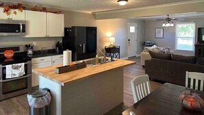A modern kitchen with a central island, a dining area with a wooden table, and a living room with a sofa and a TV.
