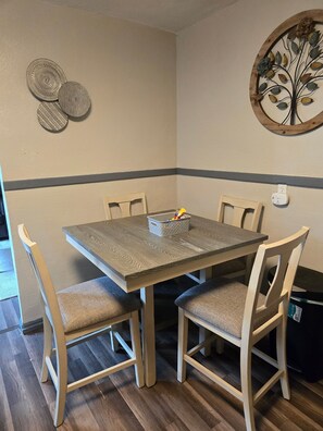 Ein Essbereich mit einem quadratischen Tisch, vier Stühlen, einem Wanddekor und einer Steckdose.