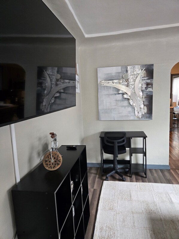 A room with a large mirror, a black desk with a chair, a white rug, and two abstract paintings on the wall.