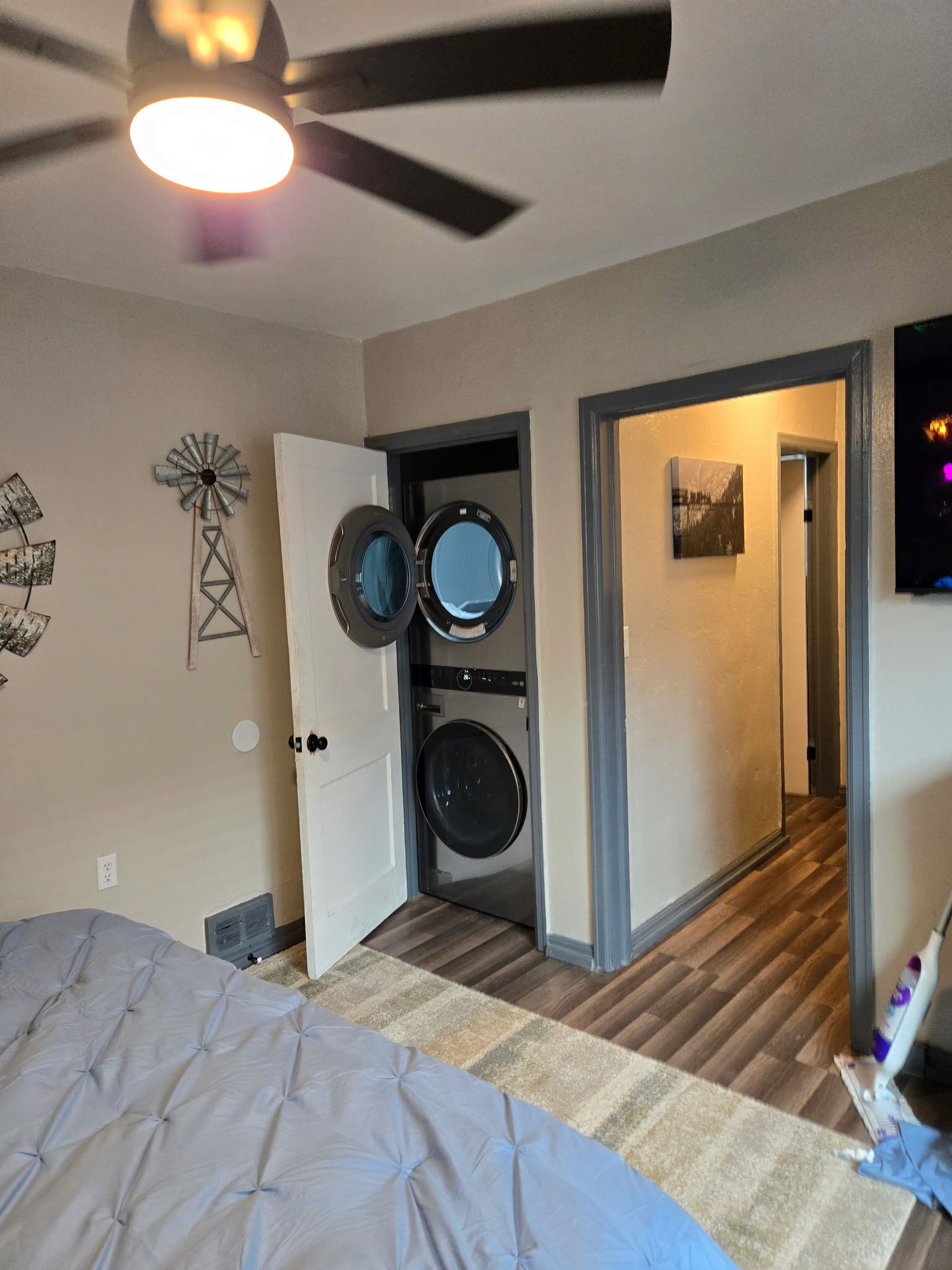 A bedroom with a bed, a ceiling fan, a washing machine, and a door leading to another room.
