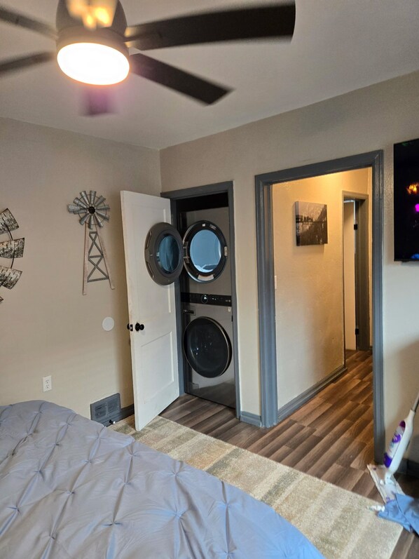 Un dormitorio con cama, ventilador de techo, lavadora y una puerta que da a otra habitación.