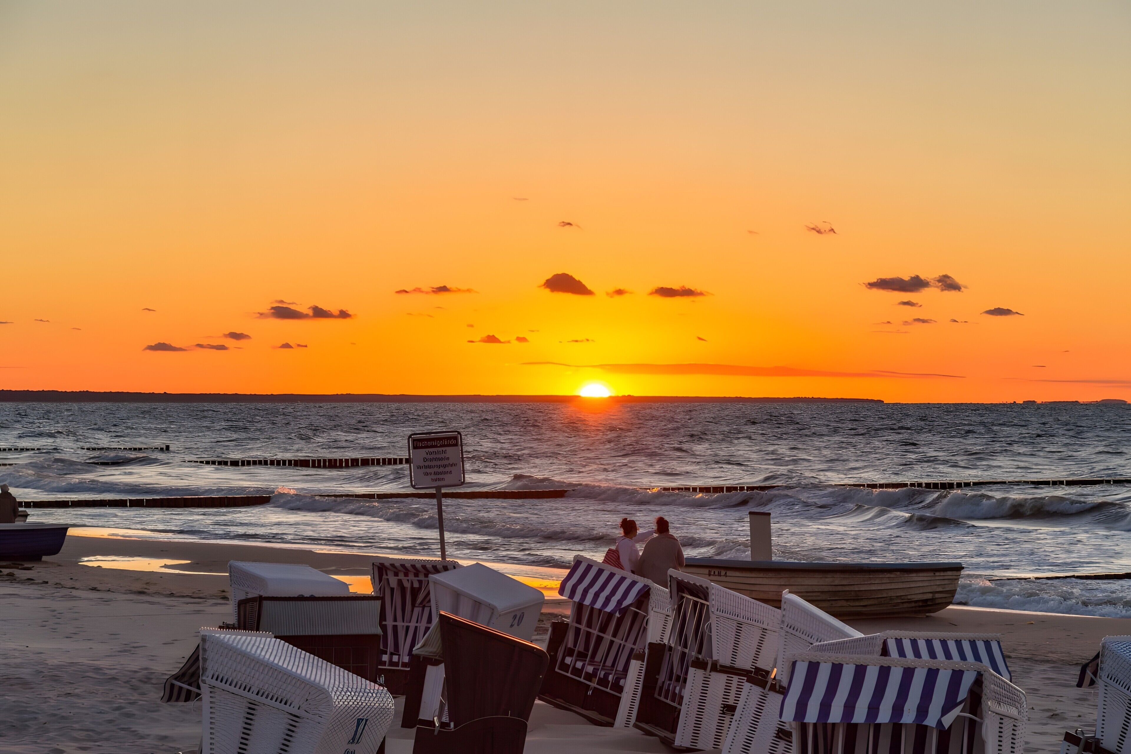 A beach scene with a sunset, chairs, and a boat.