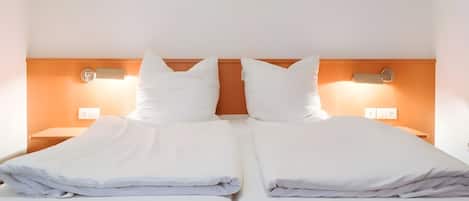 A double bed with white linens, two bedside tables, and wall-mounted lamps.