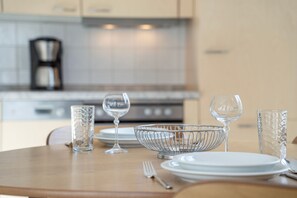 Een eettafel gedekt met transparant glaswerk en een metalen kom, met een keuken op de achtergrond.