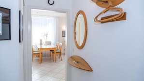 Una habitación con una mesa de comedor de madera, sillas, un espejo y piso cubierto de baldosas blancas.