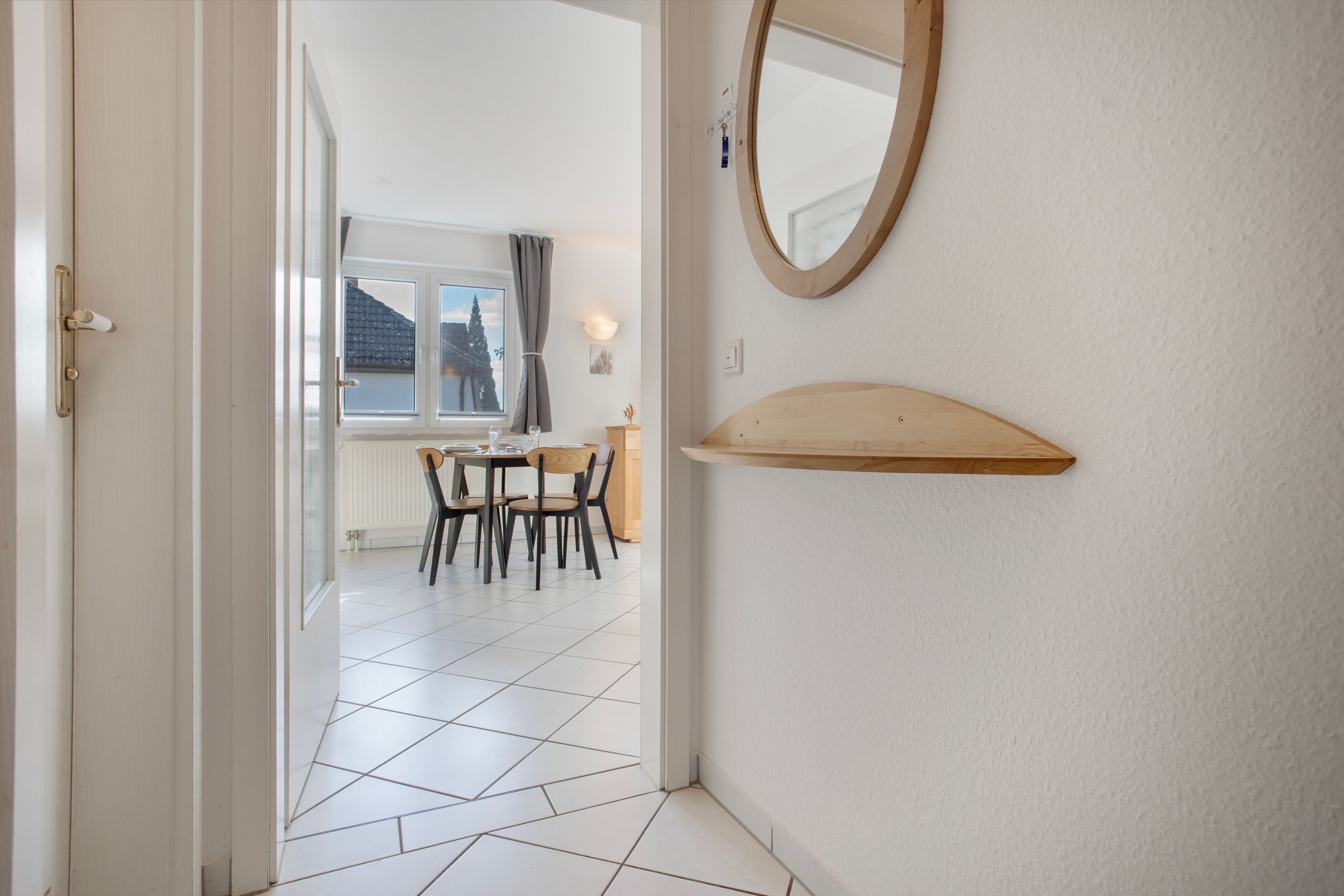 Ein Flur, der in einen Essbereich mit Tisch und Stühlen führt, mit einem Fenster mit Blick auf Bäume und einem wandmontierten Spiegel.