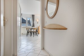 A hallway leading to a dining area with a table and chairs, a window with a view of trees, and a wall-mounted mirror. - Apartment 'Möwe' with Balcony and Wi-Fi (Zempin)