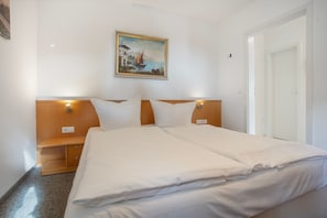 A double bed with white linens, wooden headboard, bedside tables, and a painting of a coastal scene above. - Apartment 'Möwe' with Balcony and Wi-Fi (Zempin)
