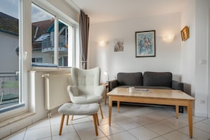 A living room with a white armchair, a grey sofa, a wooden coffee table, and a window with curtains. - Apartment 'Möwe' with Balcony and Wi-Fi (Zempin)