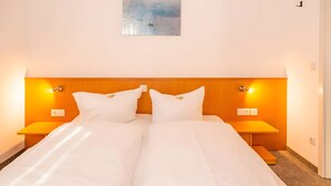 Cama doble con ropa de cama blanca, dos mesitas de noche con lámparas y un cuadro en la pared.