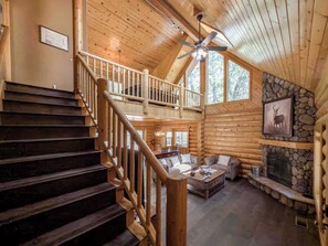 A wooden cabin interior with a staircase, a fireplace, a ceiling fan, and a dining area. - Royal Oak Bear Log Home 3BR W Game Loft (Big Bear Lake)